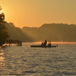 Kayak angler silhouetted on a misty lake at golden sunrise