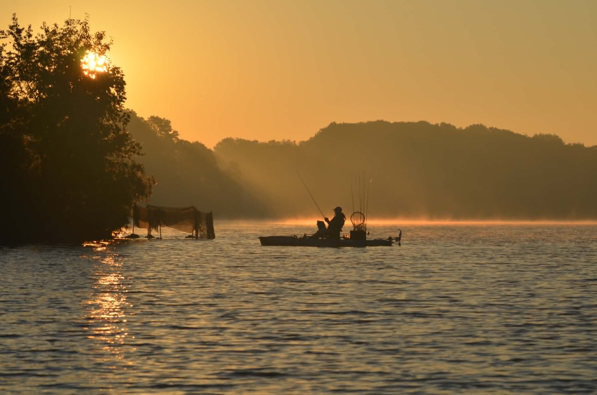 Kayak angler silhouetted on a misty lake at golden sunrise