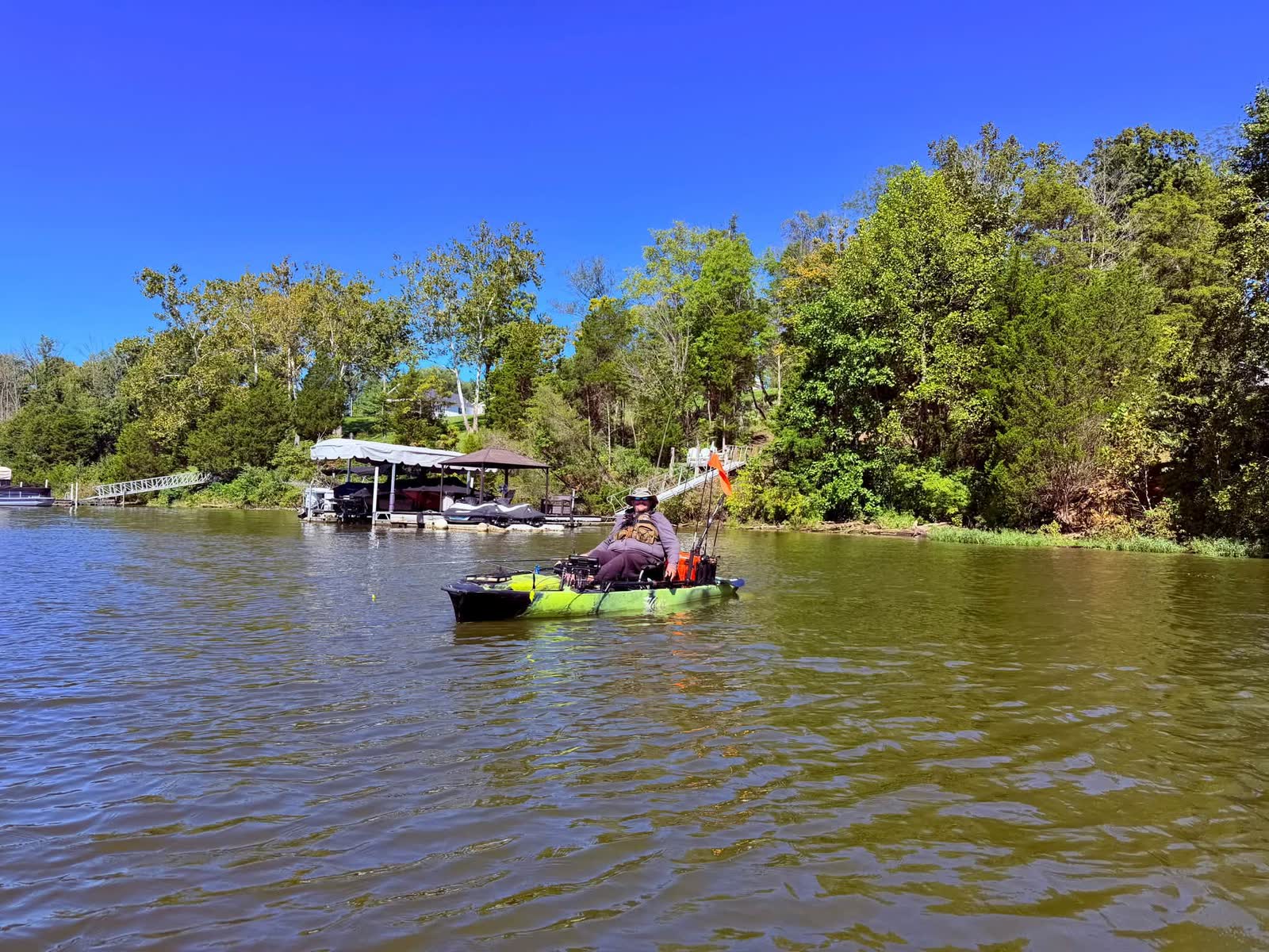 Seated kayak angler beside docks and a wooded shoreline at Rocky Fork Lake